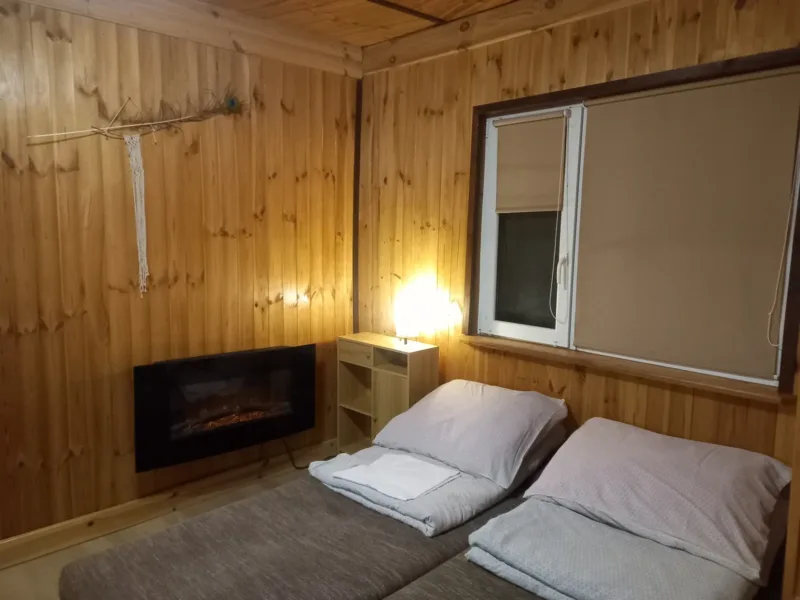Pokój w domku nr 1 z drewnianą boazerią, łóżkiem i kominkiem elektrycznym