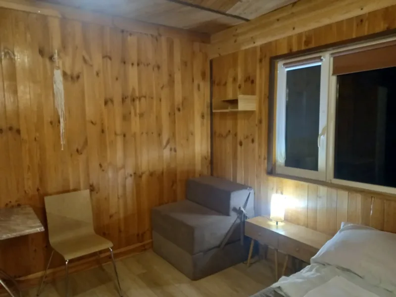 Pokój w domku nr 2 z oknem, krzesłem i łóżkiem