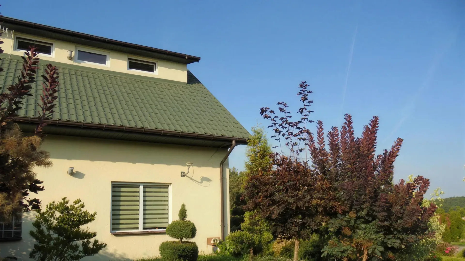 Mini pensjonat z zieloną dachówką w ogrodzie z kwitnącymi krzewami